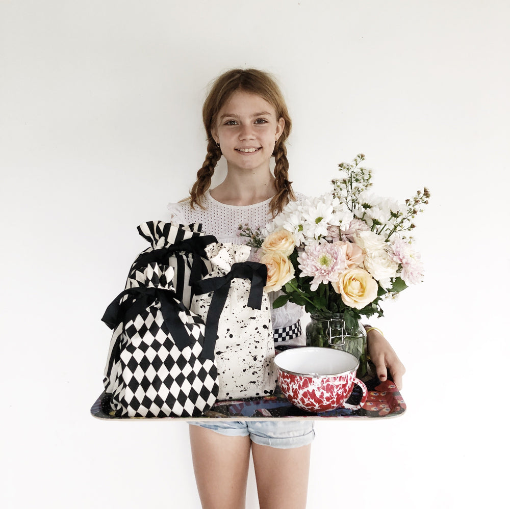 Une fille tenant un plateau avec du café, des fleurs et de nombreux sacs-cadeaux réutilisables contenant plusieurs cadeaux.
