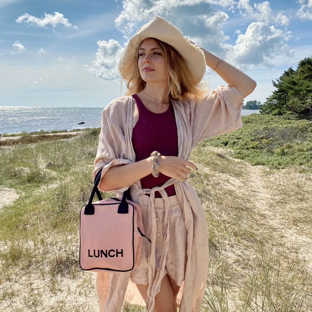 Une fille à la plage avec son sac à lunch rose.