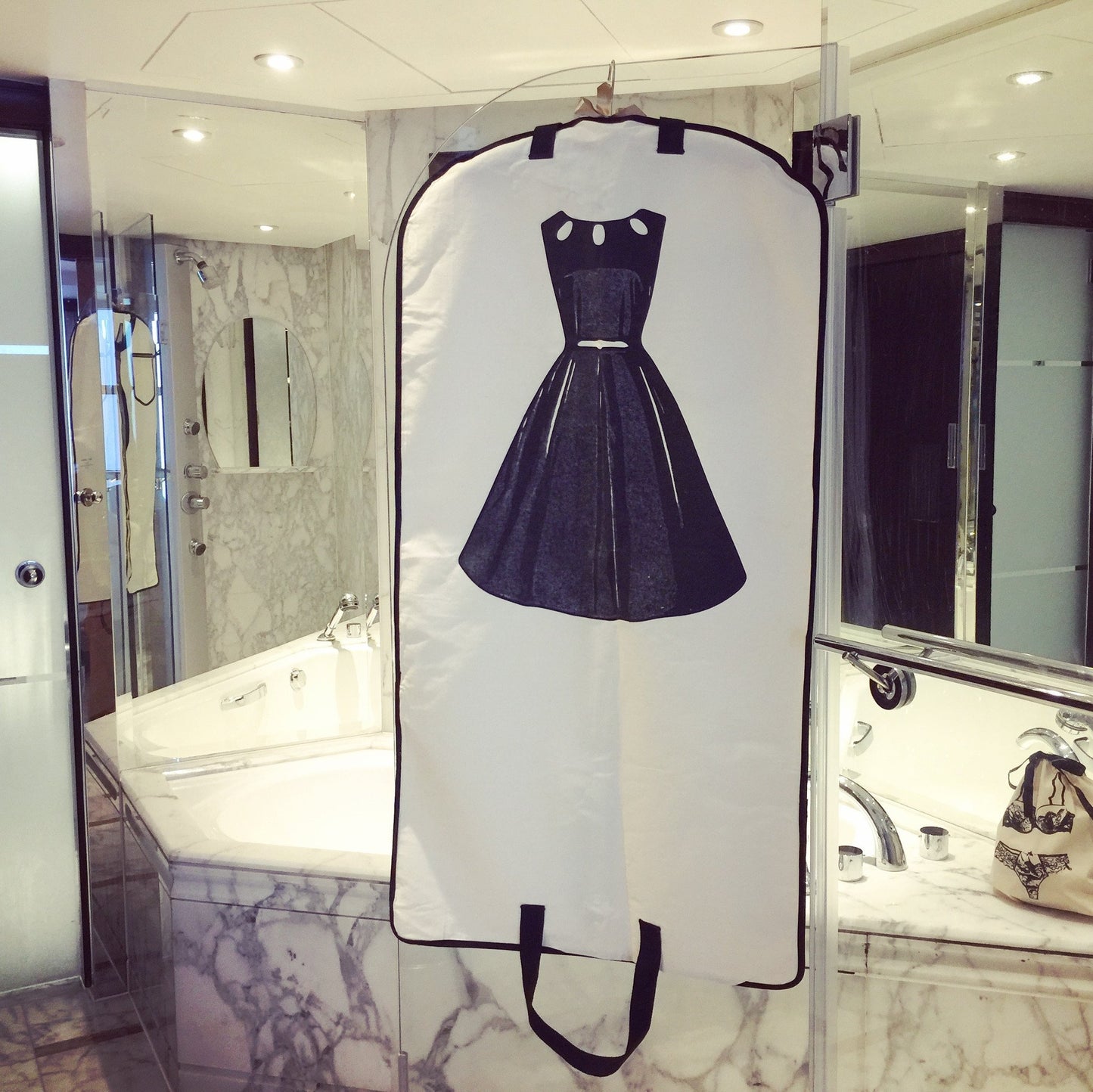 
                                      
                                        Une salle de bains en marbre avec une robe de sac à vêtements LBD accrochée à la douche.
                                      
                                    